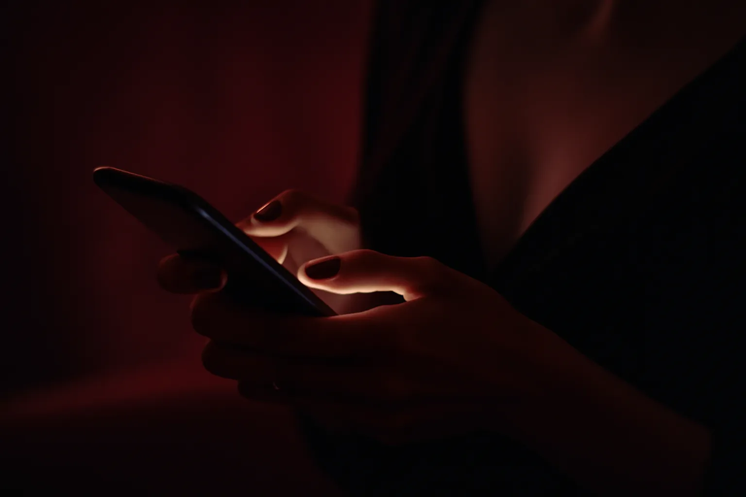 Main tenant un smartphone au message nocturne, écran lumineux, ambiance élégante bordeaux